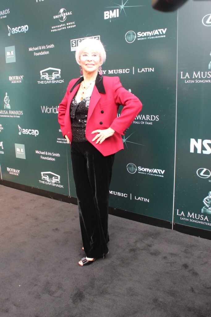 A woman in a red blazer and black trousers posing on the La Musa Awards red carpet