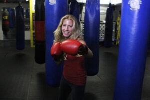 Jolie Glassman in red boxing gloves in a gym with blue punchbags