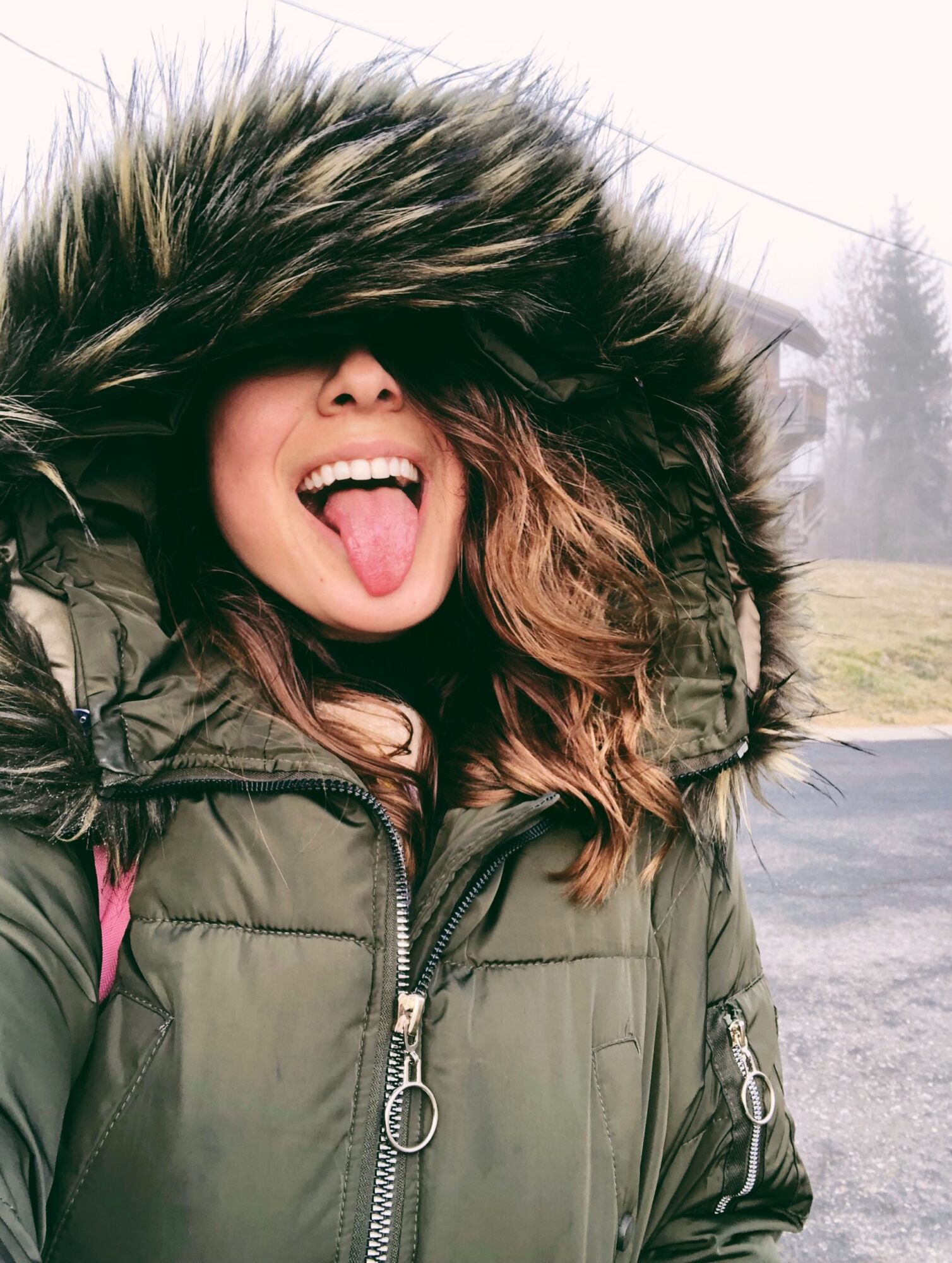 Cata pulling a face with her tongue out, the fur hood of her parka pulled up over her head