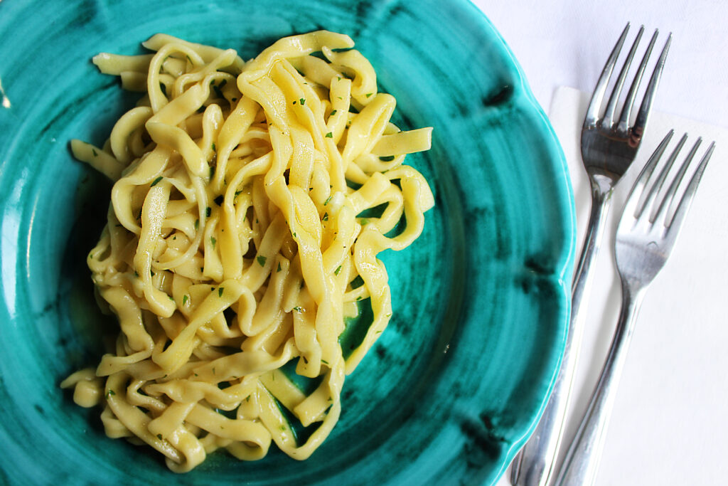 Fresh tagliatelle on a green plate beside two forks