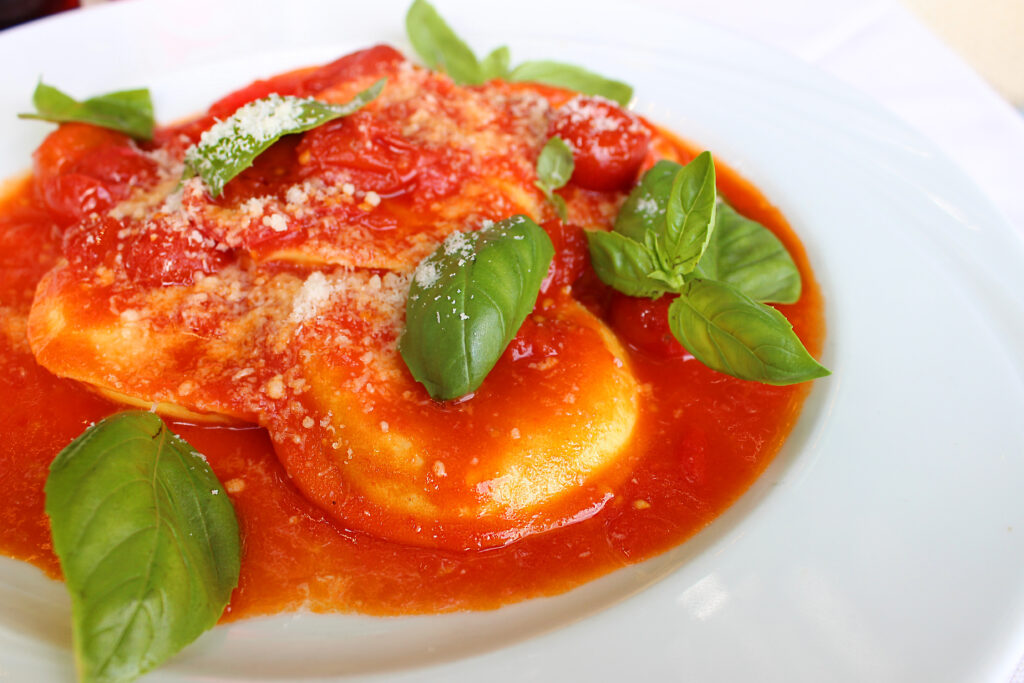 Ravioli in tomato sauce topped with grated cheese and basil leaves