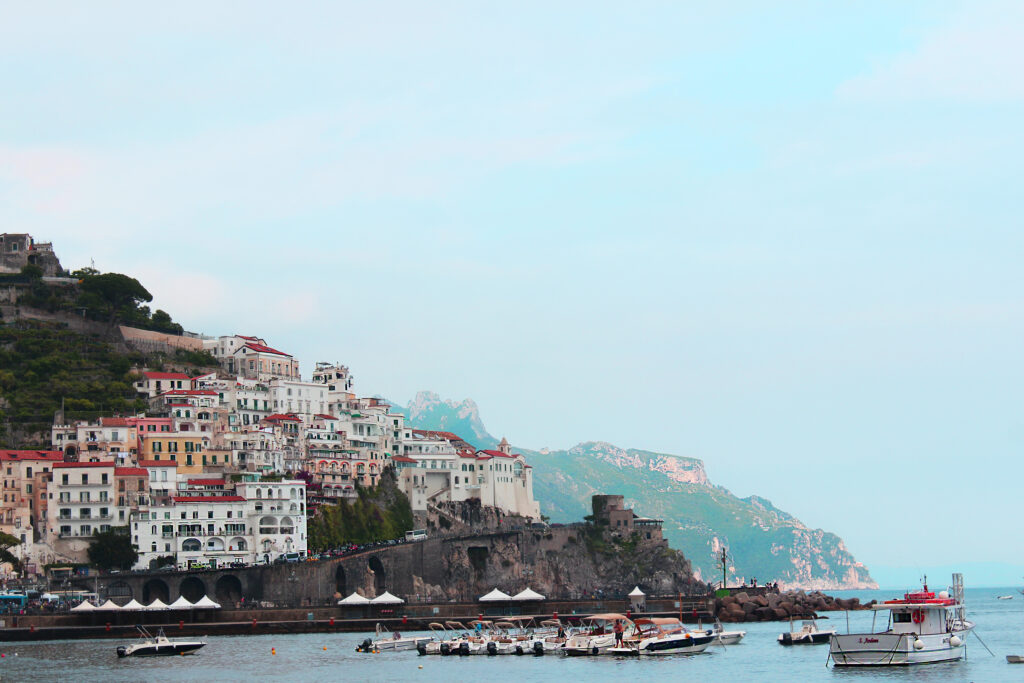 Pastel buildings on a rocky headland above the sea, boats moored below