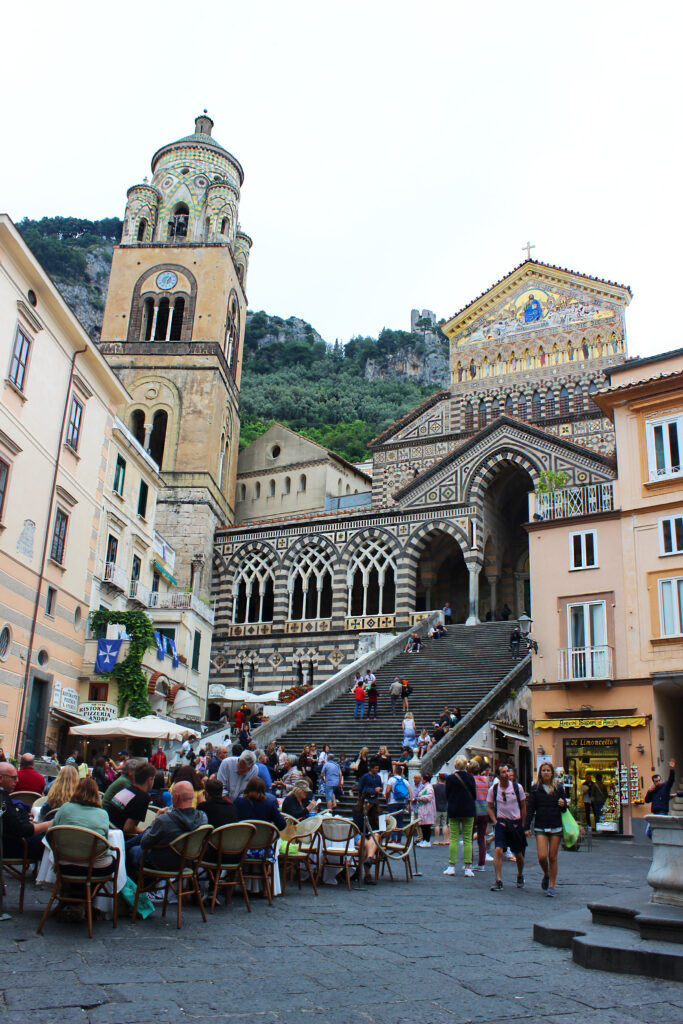 Amalfi's cathedral at the top of its wide staircase, café tables and people in the piazza below