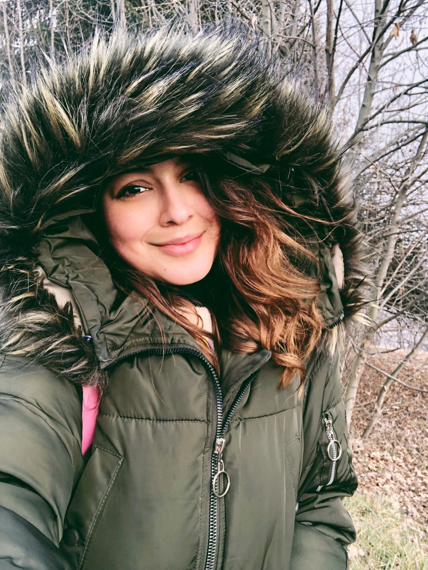 Cata in a fur-trimmed parka hood, smiling, bare winter trees behind her