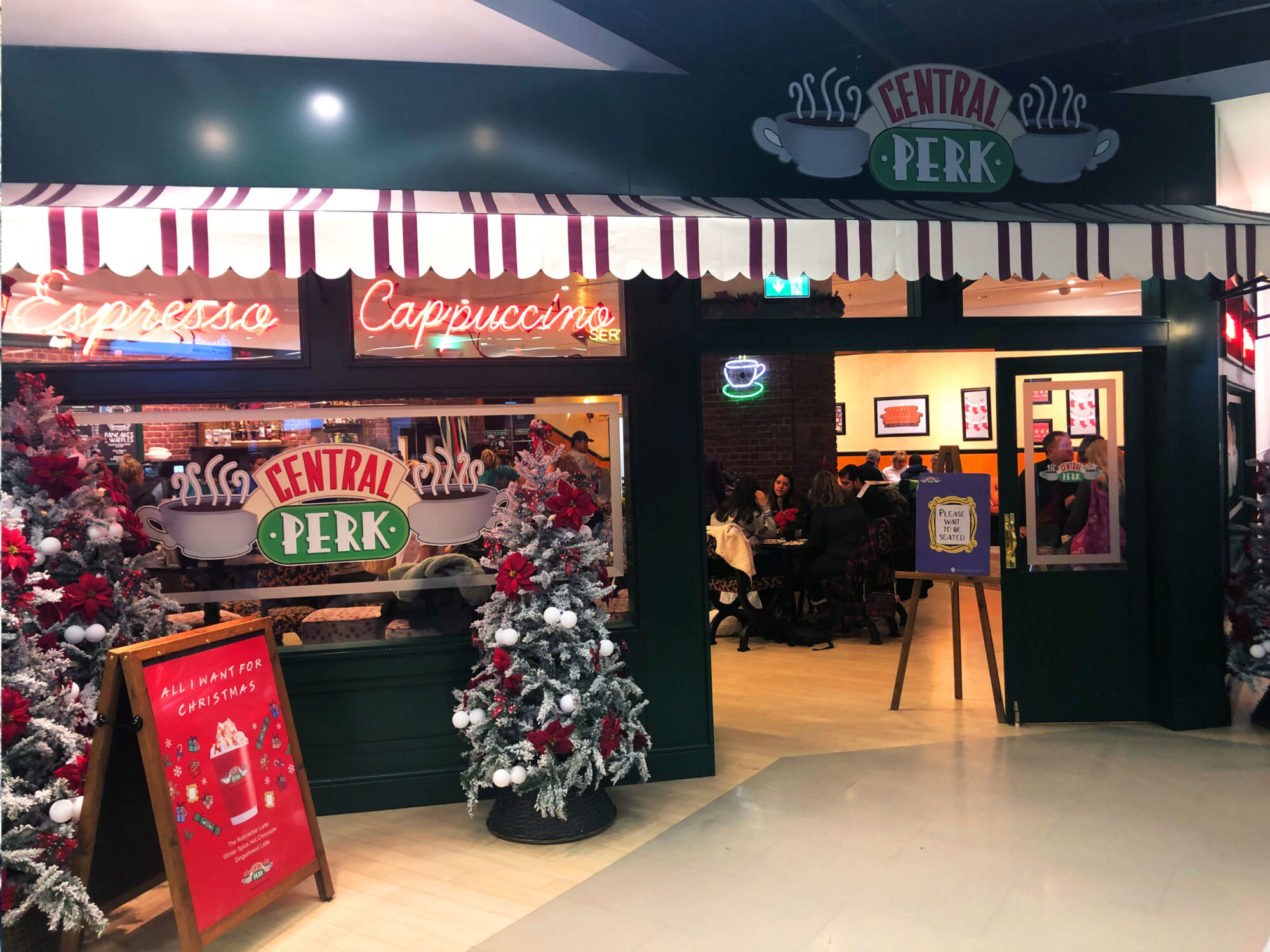 The front of The Central Perk café, decorated for Christmas with a lit Espresso and Cappuccino sign above the door