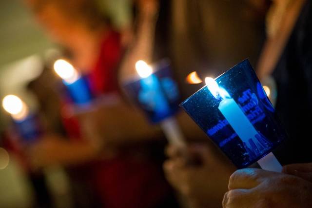 A close-up of hands holding lit candles in blue holders