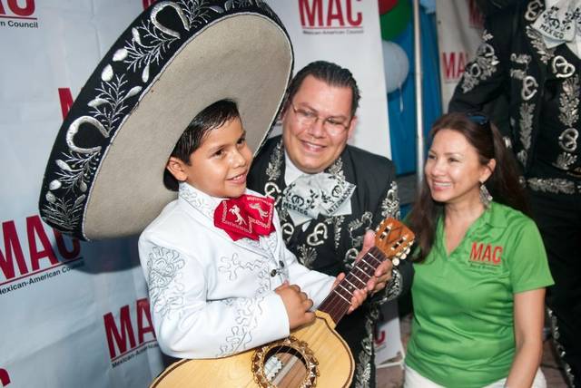 A boy in a mariachi suit and sombrero holding a small guitar, posing with two adults