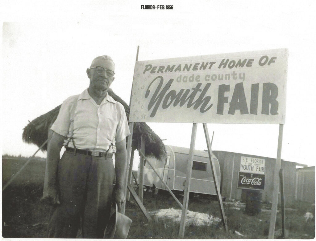 A man standing beside a sign reading "Permanent Home of Dade County Youth Fair", in an old black-and-white photo