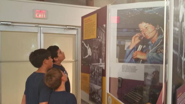 Two boys looking up at a museum panel with a large photo