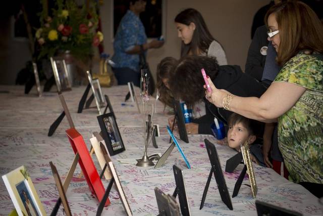 A table of framed photos of loved ones, people lighting candles beside them