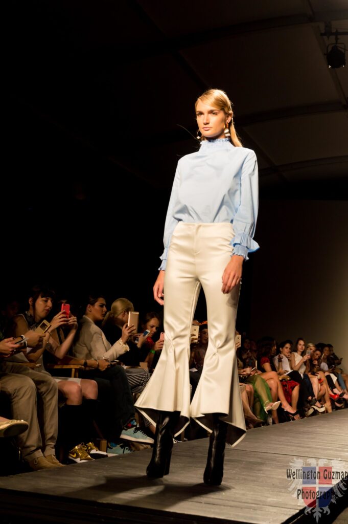 A model in a pale blue blouse and cream flared trousers on a runway
