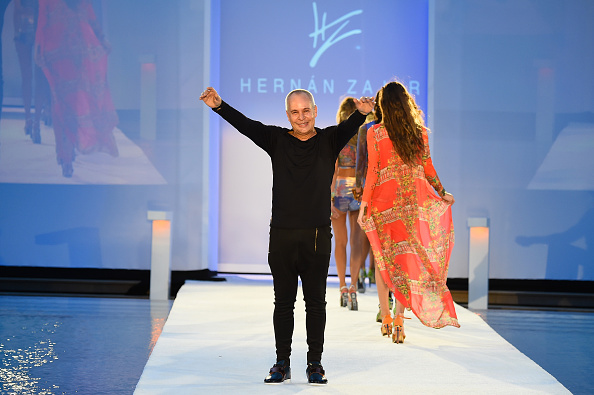 Designer Hernán Zajar waving from the end of his runway, a model in an orange kaftan beside him