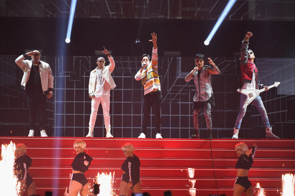 Gente de Zona, Chino, Wisin and Motiff performing on a stage lit red and white, dancers below