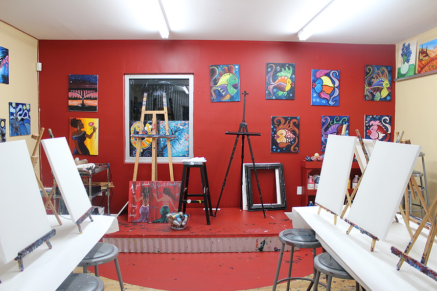 An empty painting studio with red walls, blank canvases on easels and colourful paintings hung up