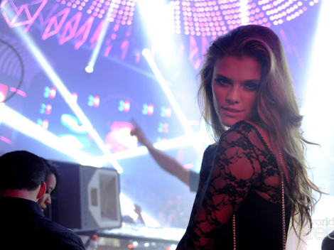 A woman in black lace at a nightclub DJ booth under coloured lights