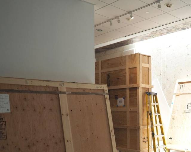 A large wooden crate and a ladder in an empty white gallery under renovation