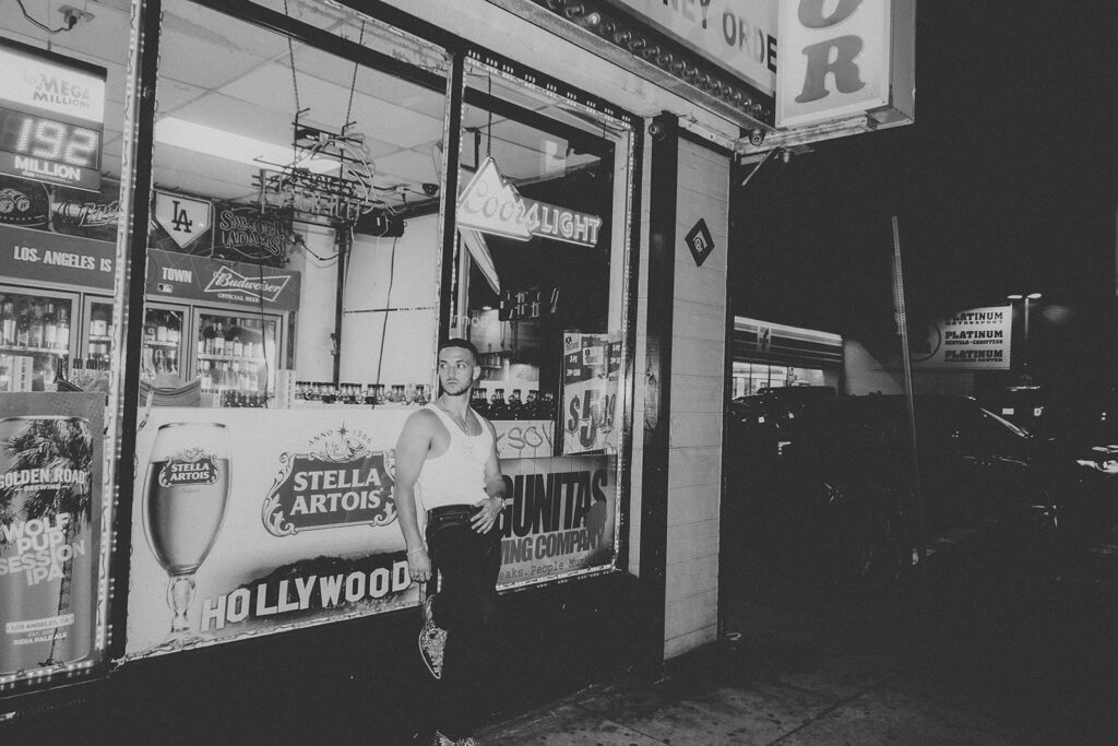 C. Tangana standing outside a liquor store at night, in a black-and-white photo