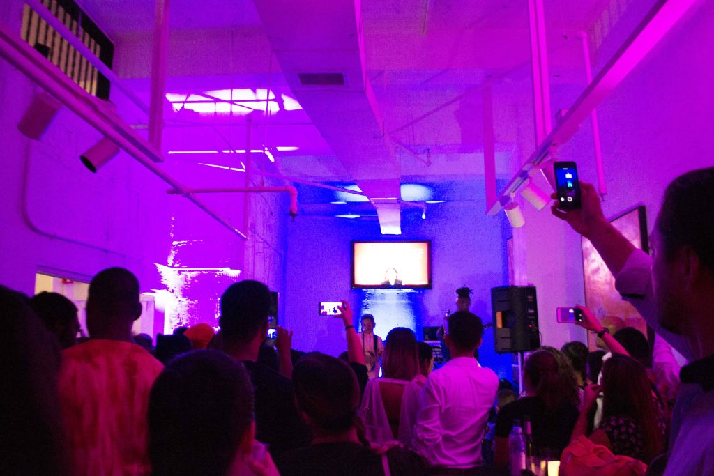 A crowd watching a performance in a room lit pink and blue