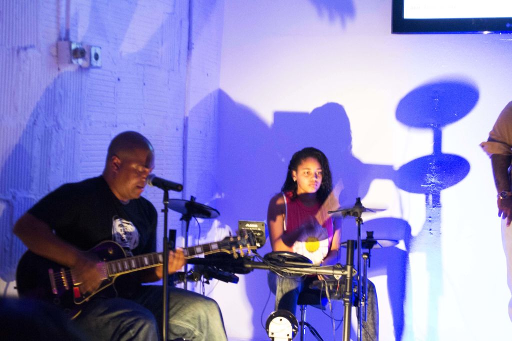 A guitarist and a young drummer performing under blue light