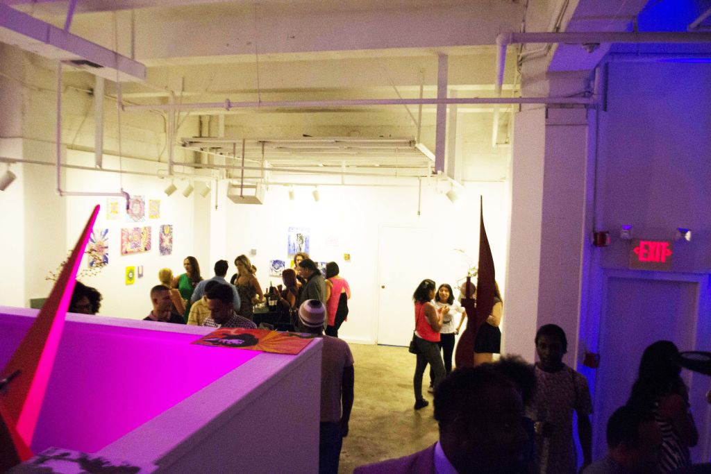 Visitors walking through a gallery lit with pink light at a student showcase