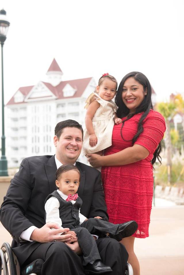 A man in a suit in a wheelchair holding a toddler, a woman in red holding another child