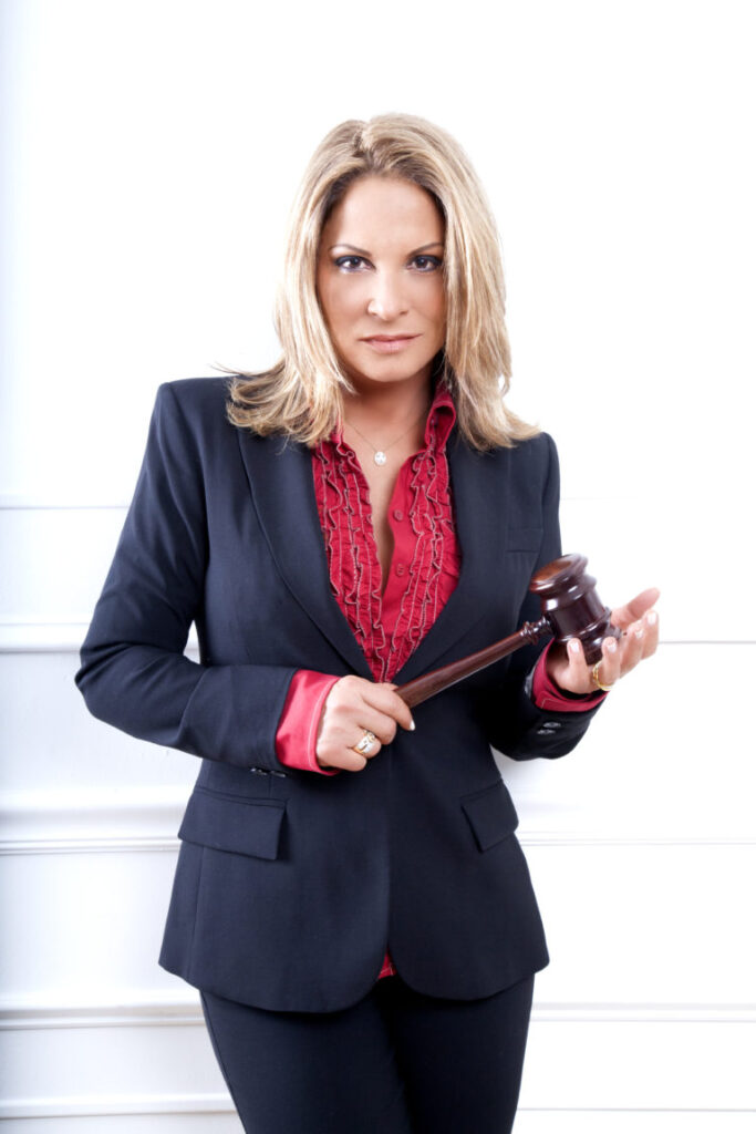 Ana María Polo in a navy suit and red shirt, holding a judge's gavel