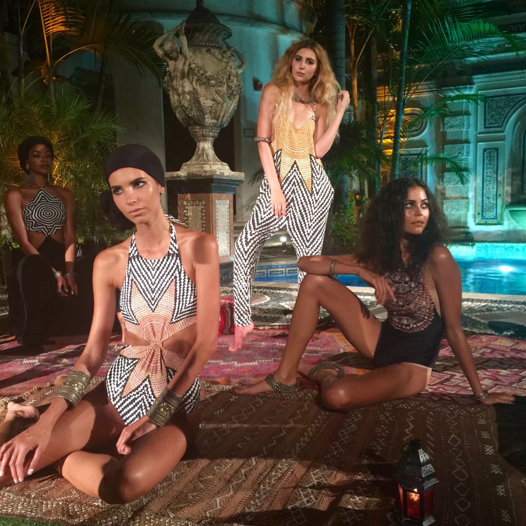 Models in swimwear lounging on patterned rugs by a garden fountain at night