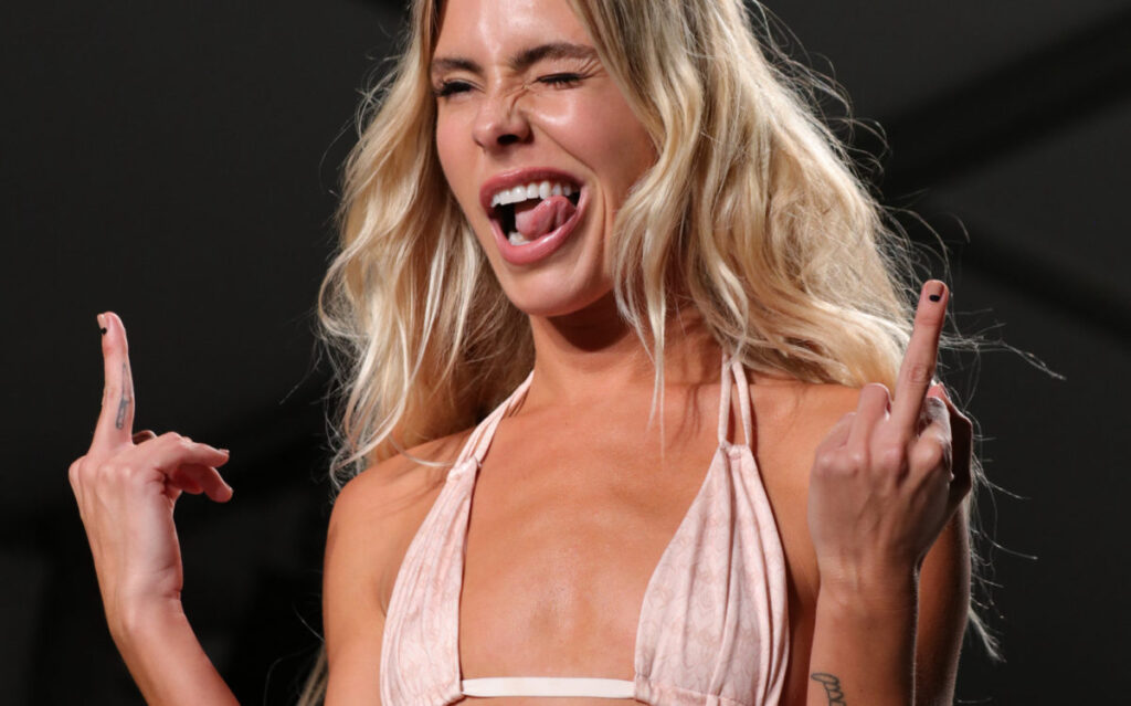 A blonde model winking and sticking out her tongue backstage at Swim Week
