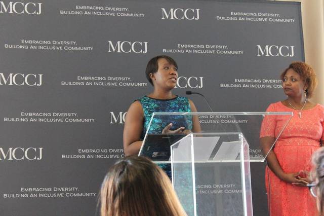 Joy Reid speaking at a clear lectern in front of an MCCJ backdrop