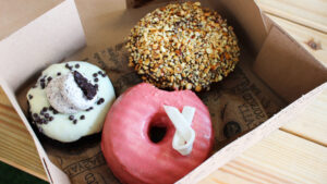 A box of three doughnuts: a cookies-and-cream, a nut-crusted and a pink-glazed one