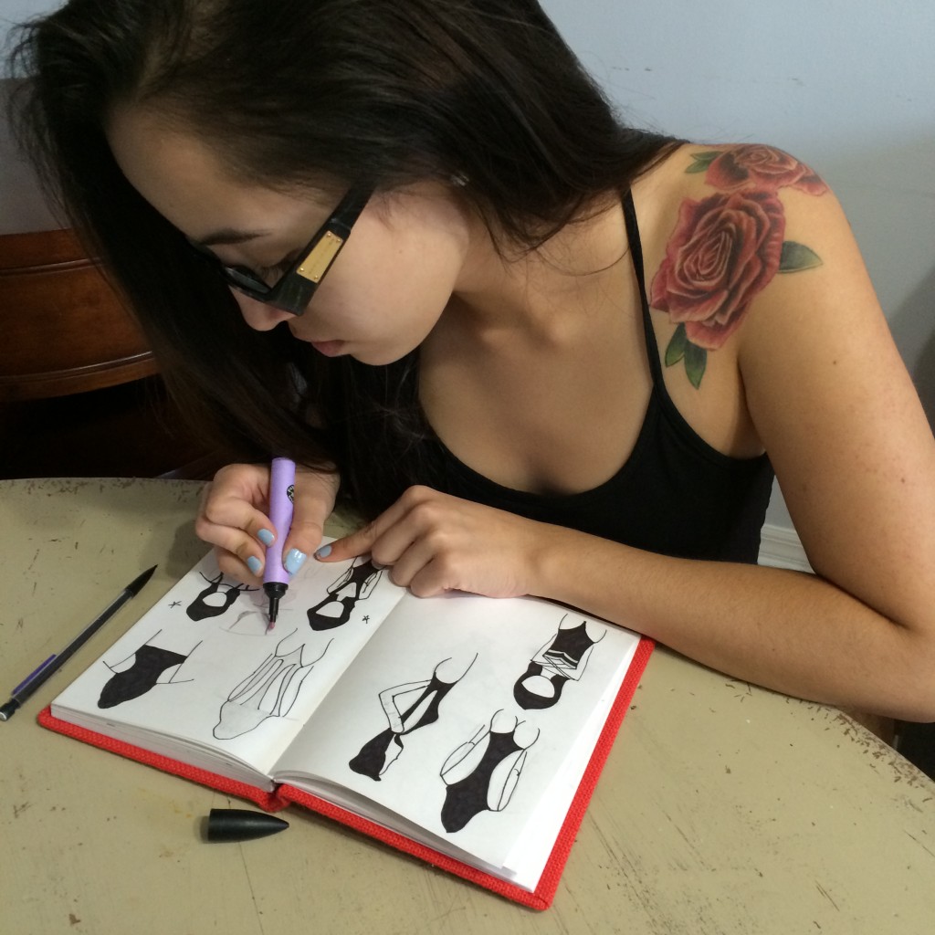 Isabella Rose, a tattooed young designer sketching swimsuits in a notebook