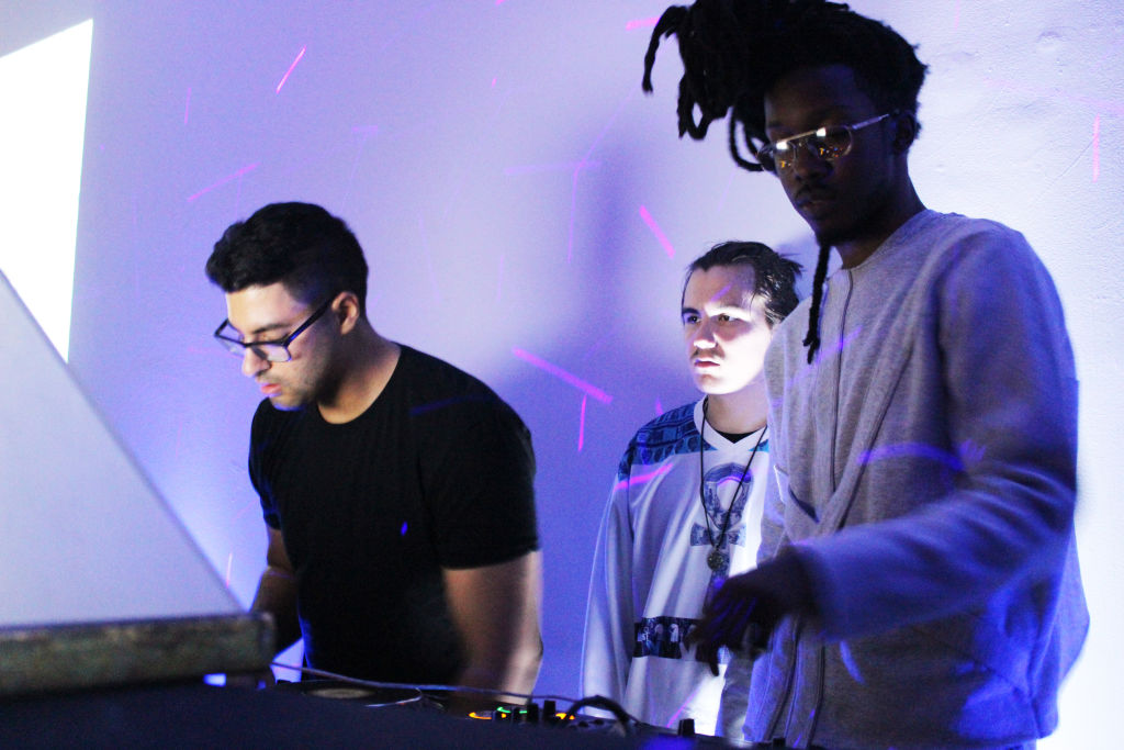 Three young men working a DJ set under blue light