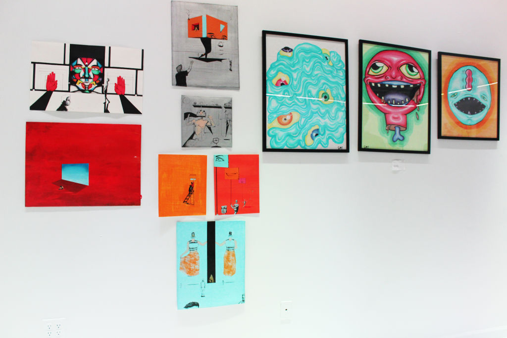 Colourful paintings, including a grinning pink face, hung on a white gallery wall