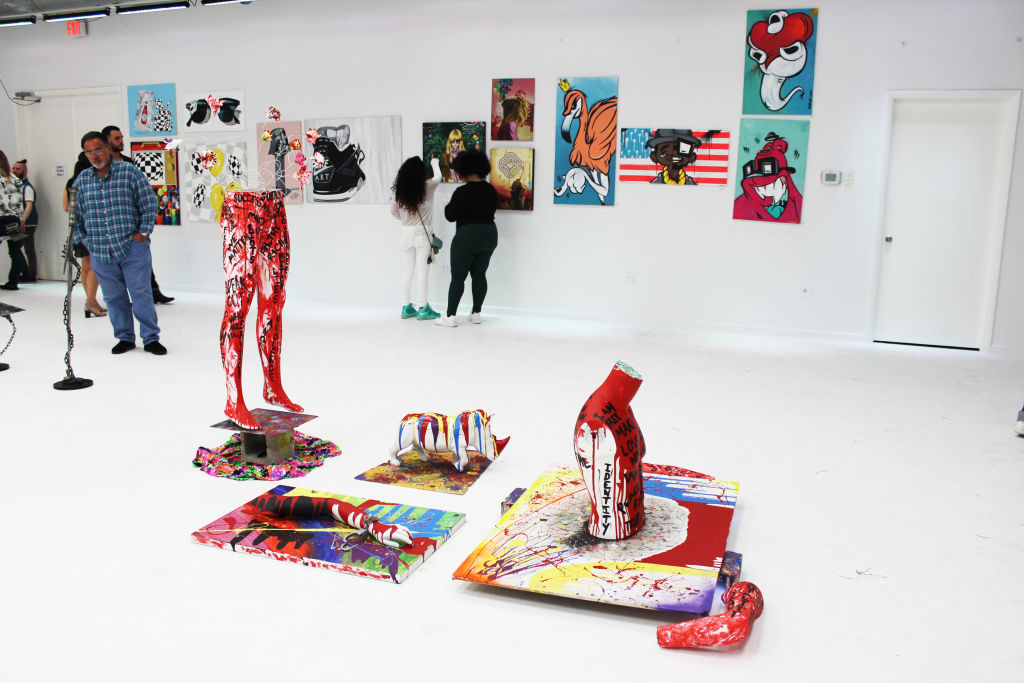 Visitors among painted mannequin legs and colourful pop art in a white gallery