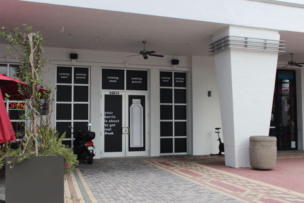The white front of a Jugofresh shop with a patio and a scooter outside