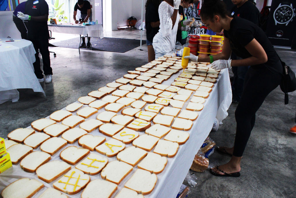A long table covered in rows of bread slices, volunteers making sandwiches