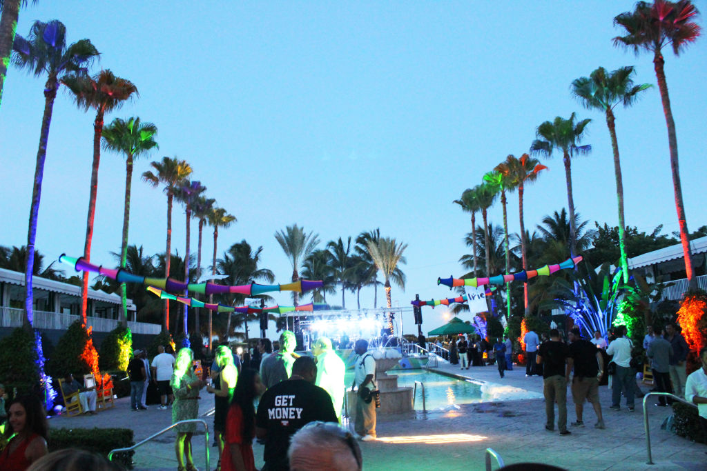 A poolside party at dusk with colourful lights strung between palm trees