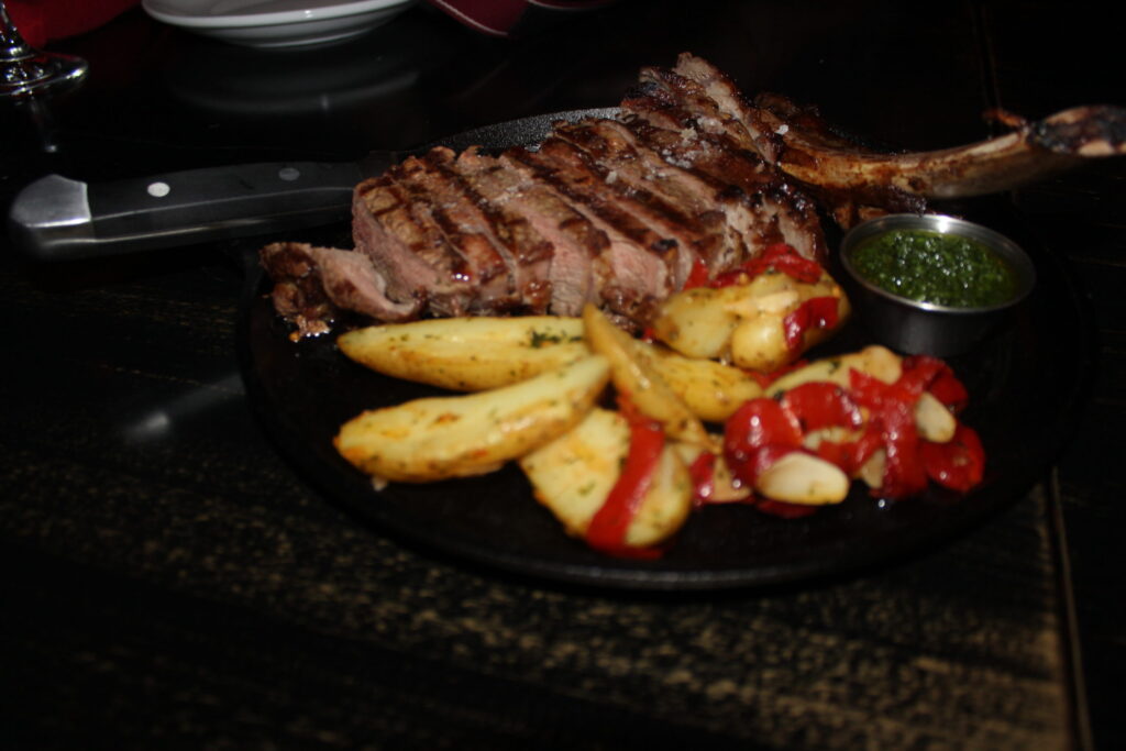 A grilled steak with roast potatoes and peppers on a black plate