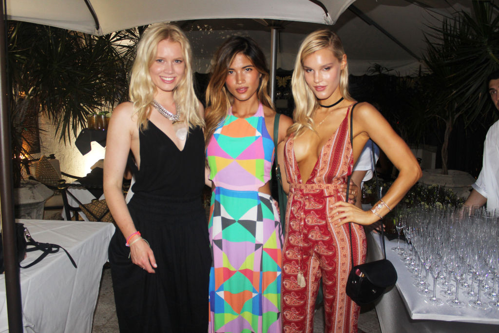 Three women in a black dress, a colourful patterned jumpsuit and a red printed jumpsuit posing at an event