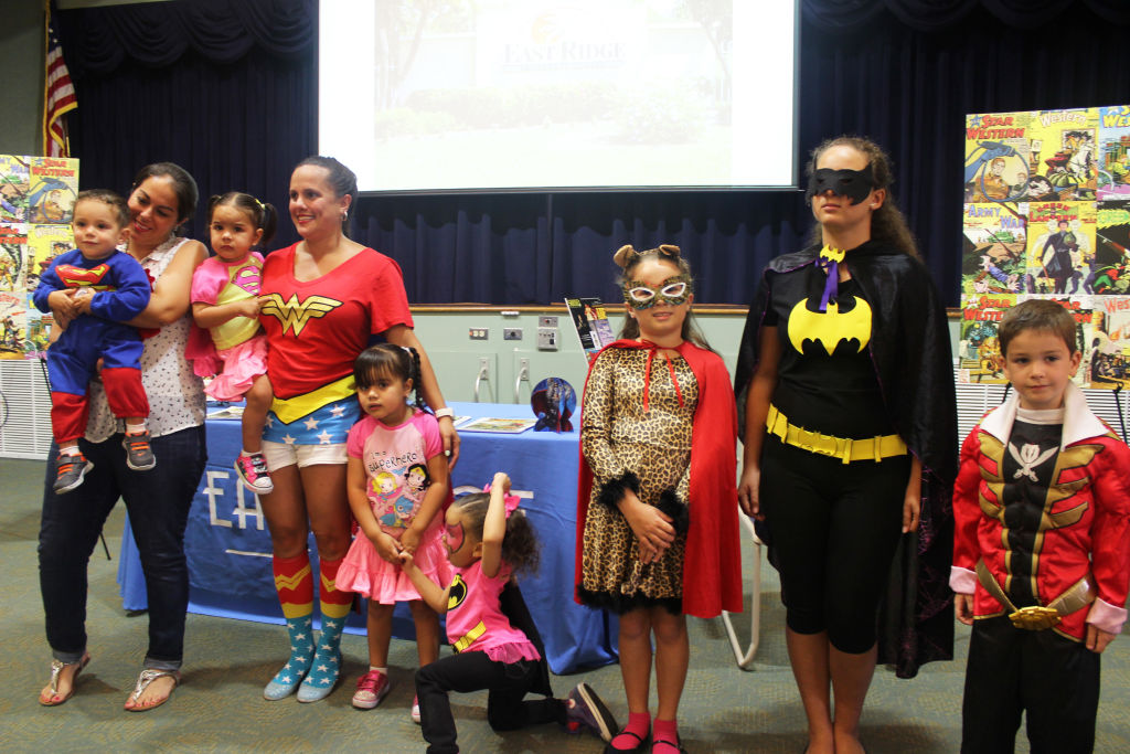 Adults and children in superhero costumes posing in front of an East Ridge table