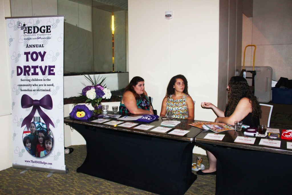 Women at a check-in table beside an EDGE Toy Drive banner