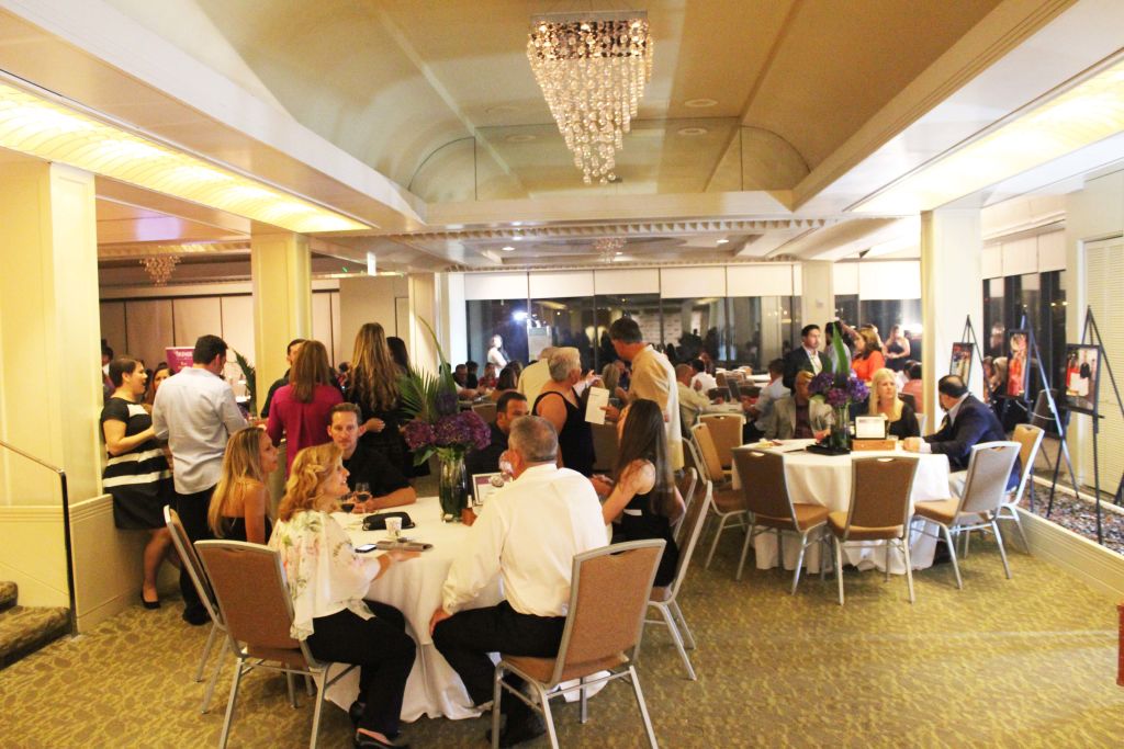 Guests at round tables in a ballroom under a chandelier at a gala