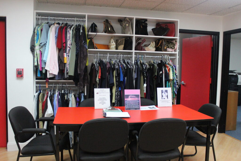 A donated-clothes room with rails of clothes, shelves of bags and a red meeting table