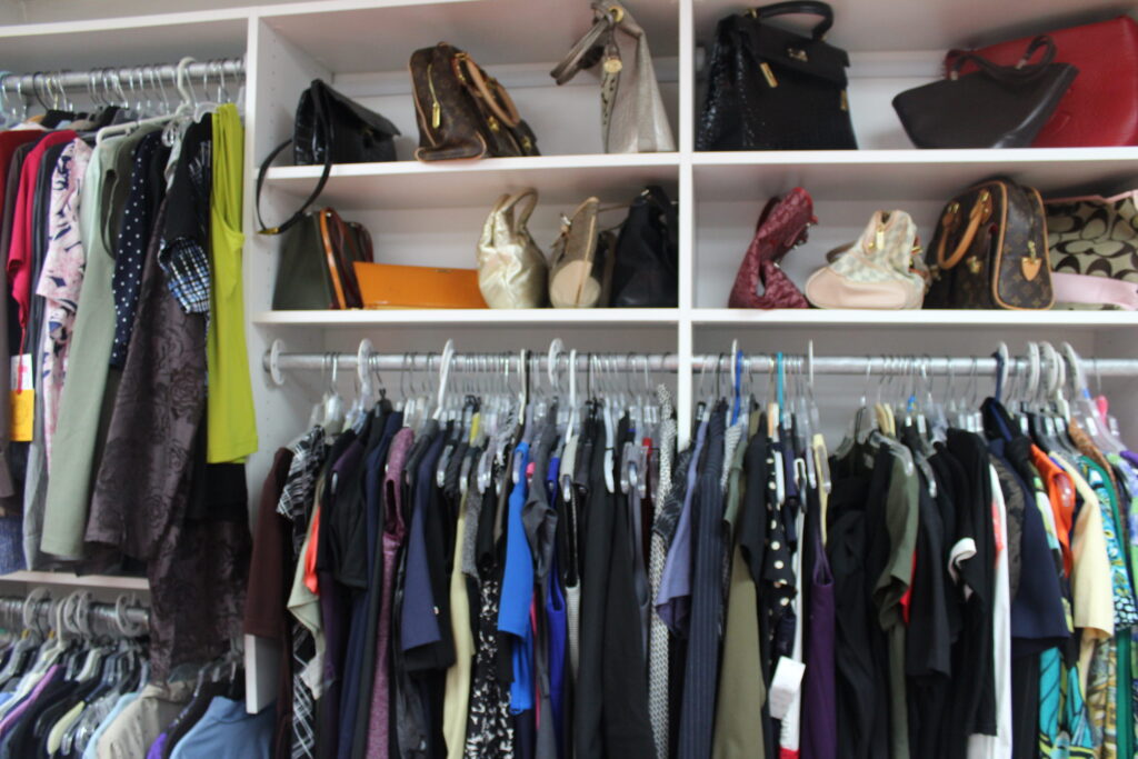 Shelves of handbags above a rail of donated clothes
