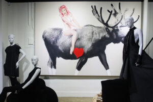Mannequins in black clothes in front of a large painting of a woman riding a reindeer