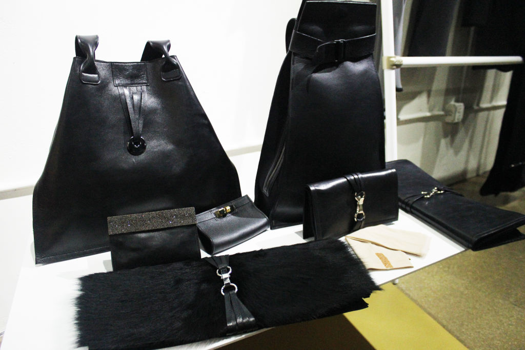 Black leather bags, a clutch and a fur piece on a white display