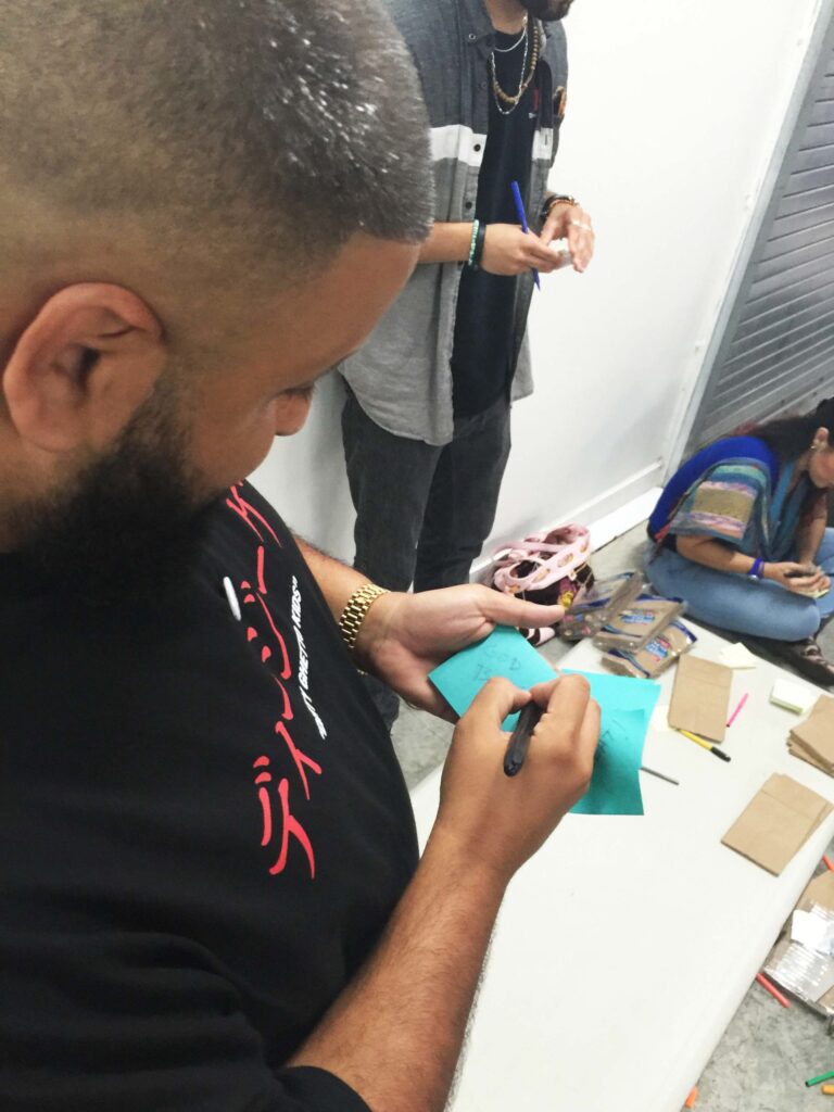 A man in a black T-shirt writing a card at a table