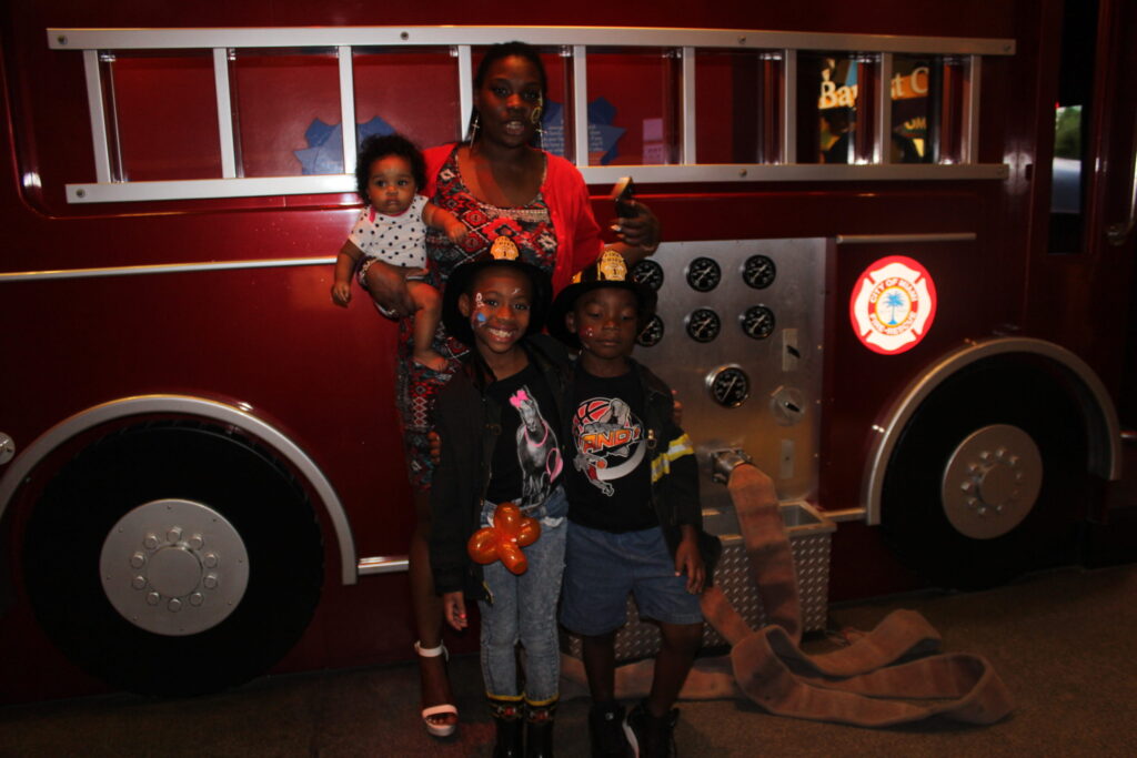 A mother and children posing beside a red fire truck exhibit