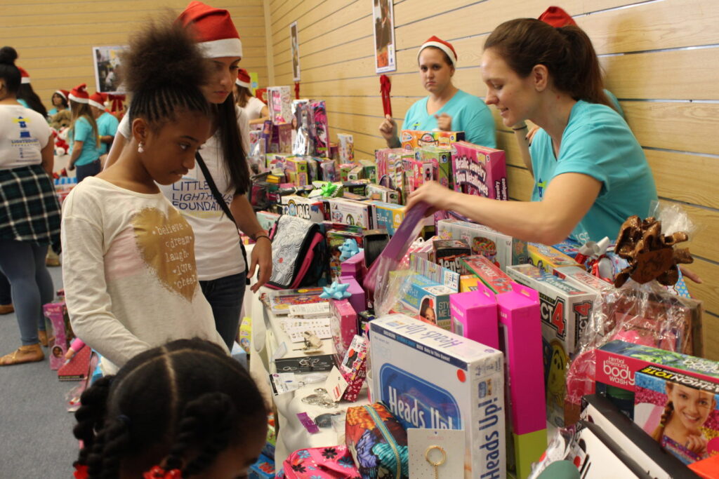 Children and volunteers at tables stacked with toy boxes at a toy drive