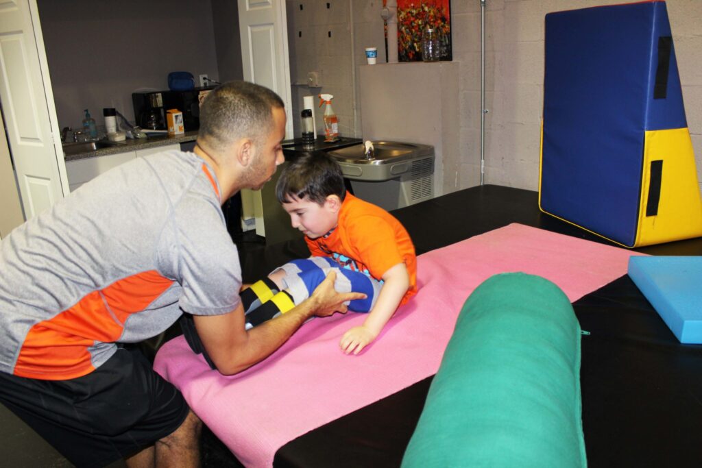 A therapist helping a young boy stretch on a pink mat